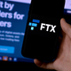 A phone with the logo FTX in front of a screen reading "Built by traders for traders."